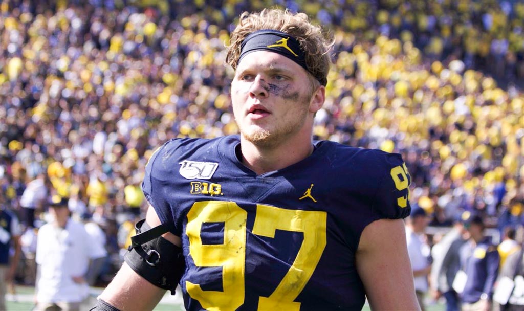Wolverines Edge rusher Aidan hutchinson stands on the field without his helmet.